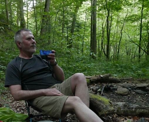 Mark Neese of True North Counseling sitting in a camping chair in the woods.