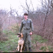 Photo of Mark Neese when he was a young Airman stationed at Rickenbaker Air Force Base, Columbus, Ohio. He was a Dog Handler tasked with guarding KC 135’s and poses with in uniform with his dog by his side.